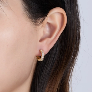 Macro shot of gold huggie earrings with baguette-cut cubic zirconia on a female ear