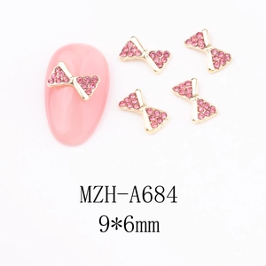 Detail of 9x6mm gold bow nail art charm with pink rhinestones for festive manicure