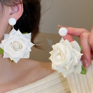Detail view of handmade white fabric rose earrings with small green leaf accents