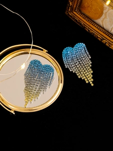Detail of gradient rhinestone heart fringe earrings with long tassel on black velvet