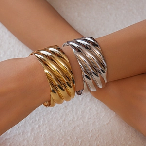 Detail of wide wave texture open bangles in gold and silver finish on model's arms