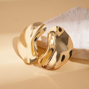 Polished gold irregular wavy earrings displayed on a marble stone backdrop