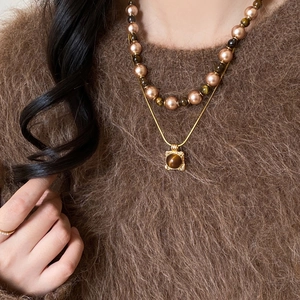 Detail of layered gold necklace with tiger eye pendant and brown pearls on sweater
