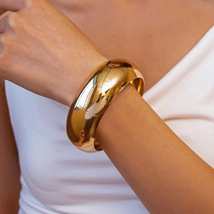 Close-up of a wide polished gold metal cuff bracelet worn on a model's wrist