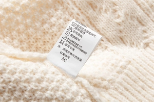 Dettaglio dell'etichetta di lavaggio su maglione a trecce bianco con istruzioni