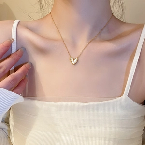Close-up of a gold chain necklace with a heart-shaped mother of pearl pendant on a model