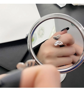 Mirror reflection showing a polished silver butterfly open ring on finger