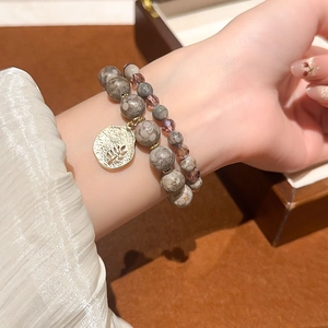 Detail of double-layer beaded bracelet with purple crystals and gold leaf charm on wrist