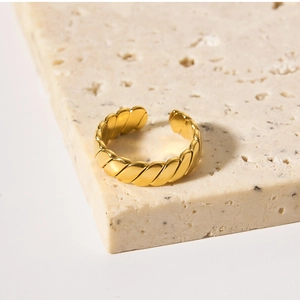 Macro shot of gold twisted metal ring with geometric texture on beige stone base