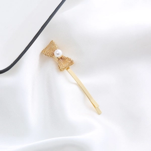 Close-up of a golden bow hair clip with a white pearl on white silk fabric