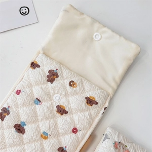Detailed macro view of quilted cream fabric storage bag with bear pattern and snap button