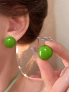 Close-up of bright green glossy spherical stud earrings for a fresh dopamine look