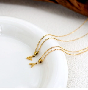 Close-up of golden necklace featuring letter V and A pendants on a white porcelain dish