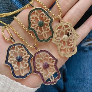 Macro detail of copper Hamsa hand pendant with colorful zircons on a gold chain