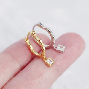 Close-up of irregular textured silver earrings with square crystals in gold and silver