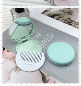 Detail of mint green cookie-shaped pocket mirror and white comb on an open book