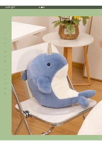 Detail view of narwhal plush toy with golden spiral horn on a white folding chair