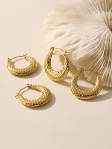 Macro detail of U-shaped gold earrings with honeycomb texture on coral props