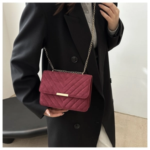 Detail of burgundy V-quilted faux suede crossbody bag with elegant gold chain strap