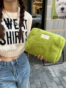 Green plush fleece makeup storage bag with white minimalist label shown in a street setting