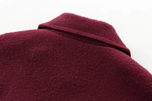 Gros plan sur la texture en laine tweed bordeaux et les finitions d'une veste courte