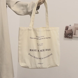 Beige canvas tote bag with black typography print shown in a minimalist lifestyle setting