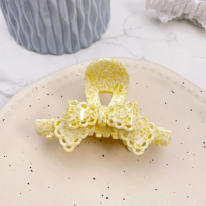Detailed top view of a yellow and white hollow grid bow hair claw on a beige ceramic plate