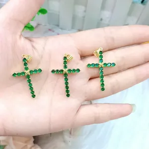 Close-up of 18K gold cross pendants with emerald green stones held in hand