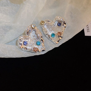 Detailed macro view of silver heart earrings with irregular lava texture and colored crystals