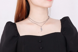Detail of layered silver wing pendant necklace on a model with paperclip chain link