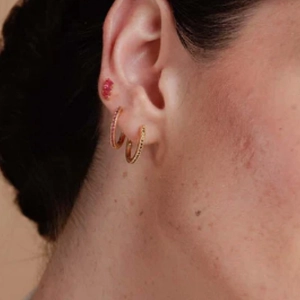 Close-up of red and blue zircon gold earrings worn on earlobe in a stacked style