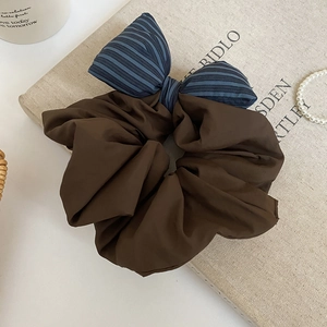 Detailed view of deep brown pleated hair scrunchie with blue-black striped bow on book