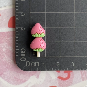 Detailed view of pink resin strawberry charm measured at 3.5cm on a scale grid