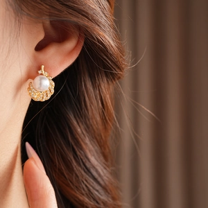 Close-up of golden feather earrings with pearls and pavé cubic zirconia on model's ear