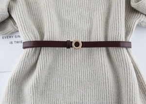Detail of dark brown slim leather belt with gold round buckle on a knit sweater