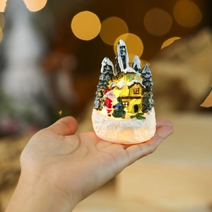 Detail view of mini LED Christmas house and Santa held in hand for scale with warm bokeh
