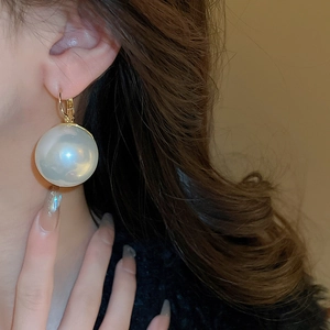 Grosse boucle d'oreille en perle blanche et fermoir doré portée par un mannequin