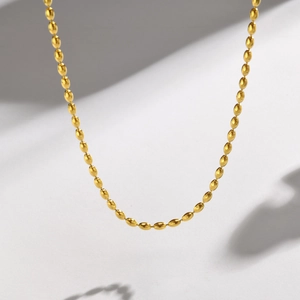 Detail of golden stainless steel oval bead necklace with soft shadow on white background