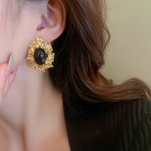 Detailed close-up of a vintage oval gold earring with black stone on a model's ear