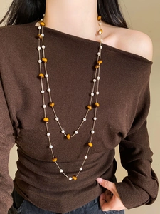 Detail of layered necklace featuring white pearls and brown tiger eye beads on model