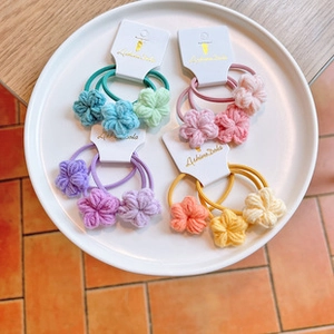 Detail of four sets of colorful handmade crochet flower hair ties on a white display tray