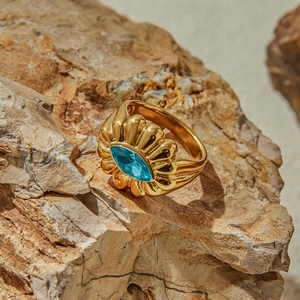 Detail of a wave-textured gold ring with oval blue gemstone on a natural rock surface