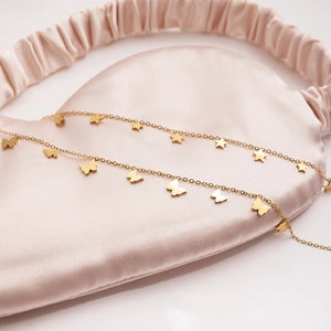 Detail of 18K gold stainless steel butterfly and star charms on pink silk background