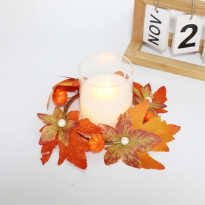 Detail of autumn candle ring with maple leaves, mini pumpkins, and a glass holder