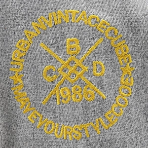 Close-up of yellow vintage embroidery with Urban Vintage text on grey baseball cap fabric