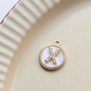 Macro detail of gold plated letter X pendant with white shell inlay and zircon stones