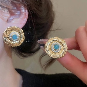 Detail of vintage gold flower stud earrings with blue gemstone and zircon halo inlay
