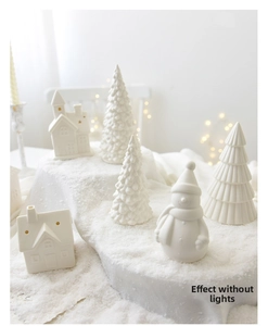 Detail of white ceramic Christmas tree and house figurines with warm starry light backdrop