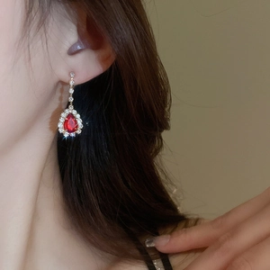 Detail of elegant gold drop earring with a red teardrop stone and shimmering crystals