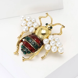 Elegant gold bee brooch with white pearls, red enamel, and green crystals on white base